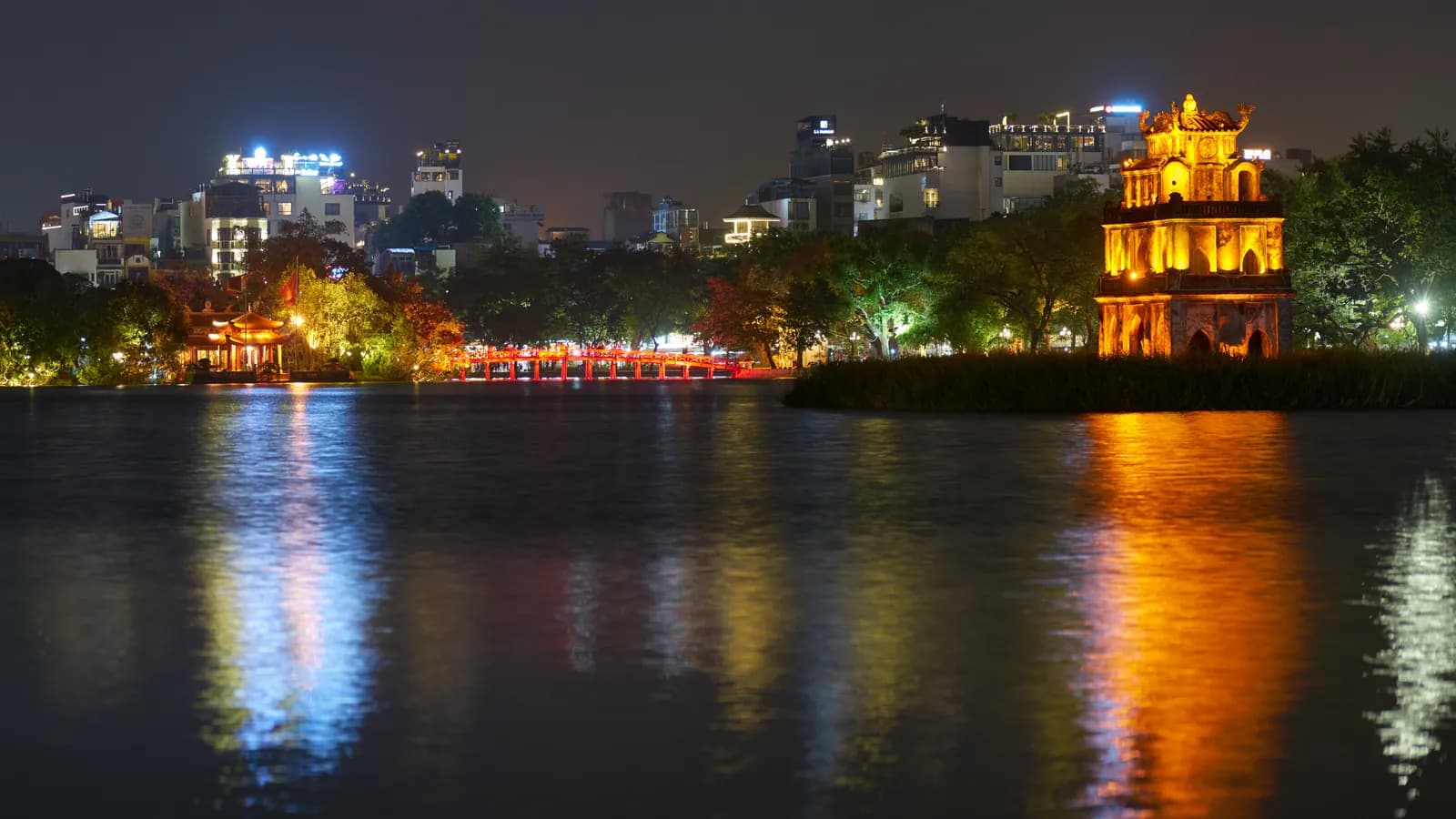 Hoan Kiem Lake in Hanoi after dark, with colorful lights reflecting across the water