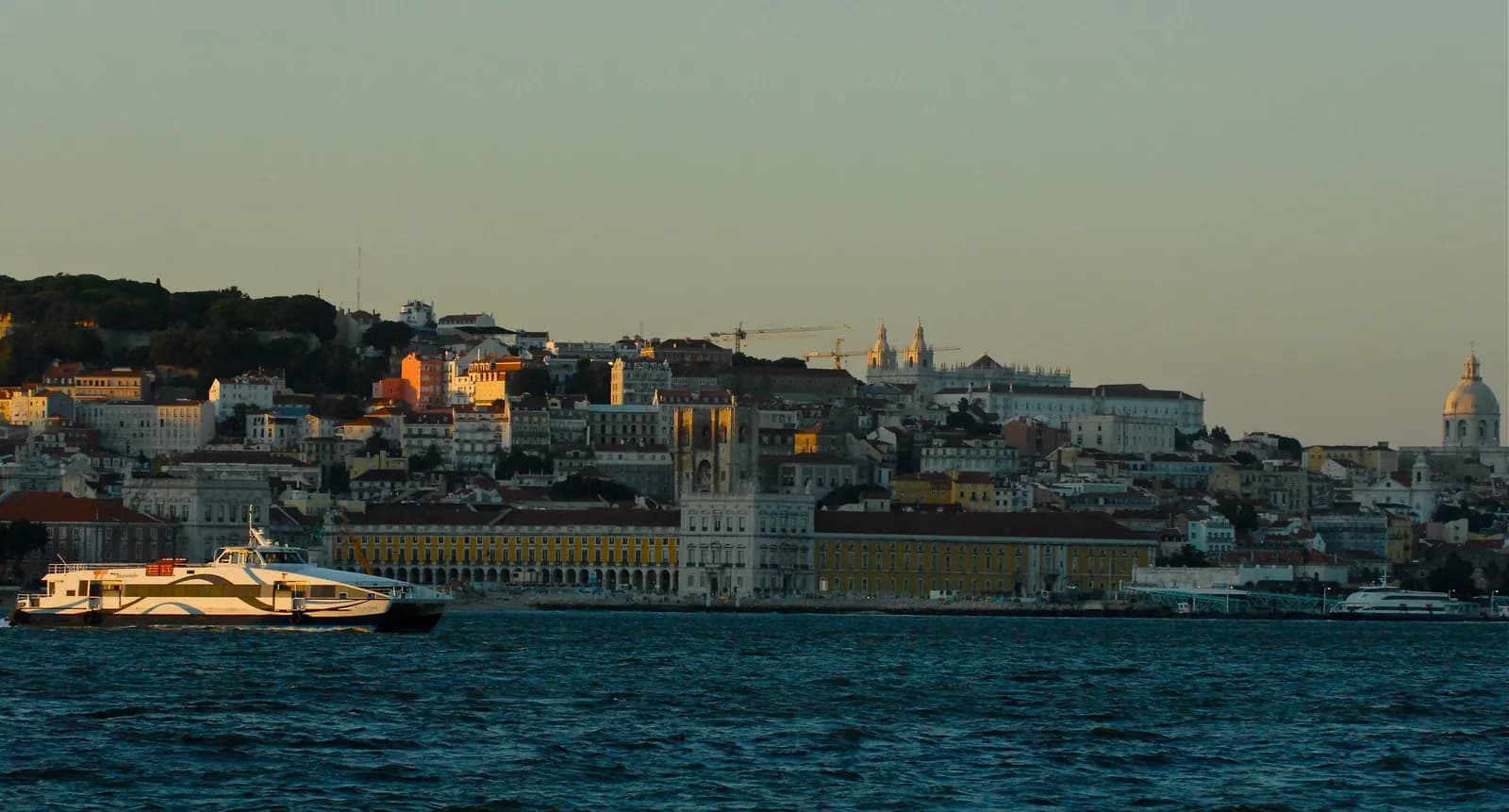 Lisbon's waterfront and hilltop buildings in evening light, seen from the Tagus River