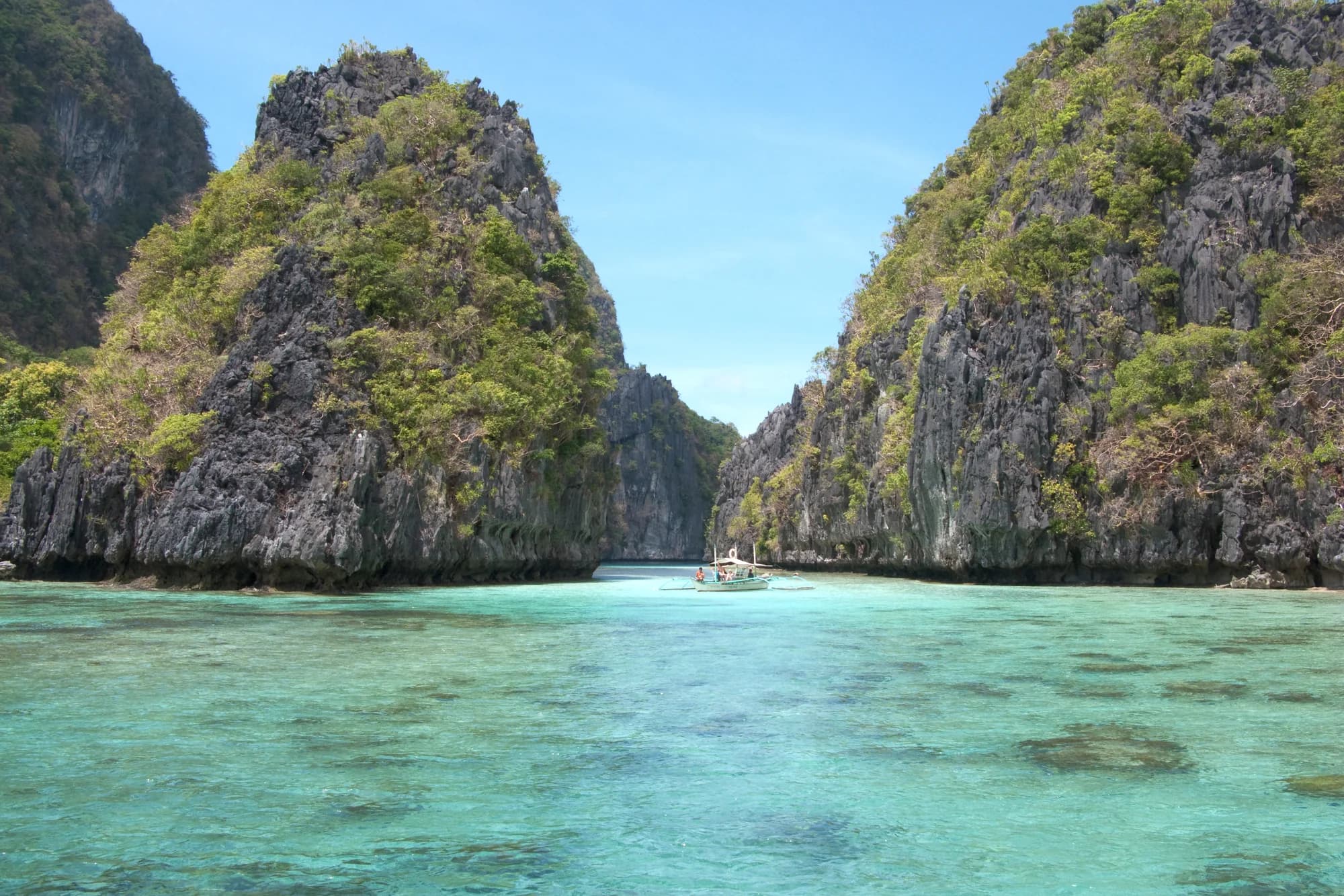 Turquoise water and an outrigger boat between limestone cliffs in Bacuit Bay, El Nido, Palawan, Philippines