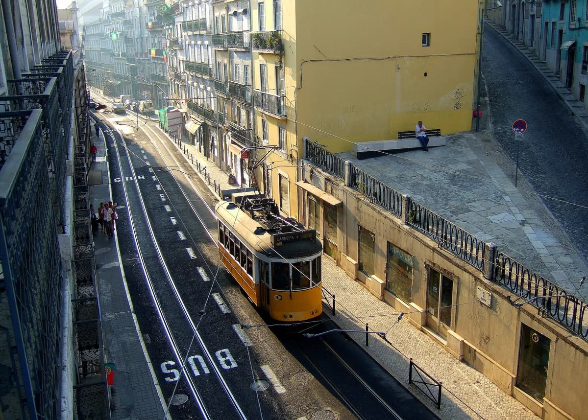 A yellow Lisbon tram traveling along a sunlit street lined with traditional buildings in Portugal