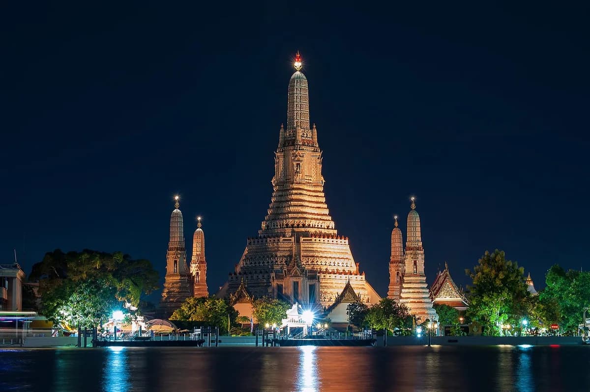 Illuminated Wat Arun temple reflected in the Chao Phraya River at night in Bangkok, Thailand